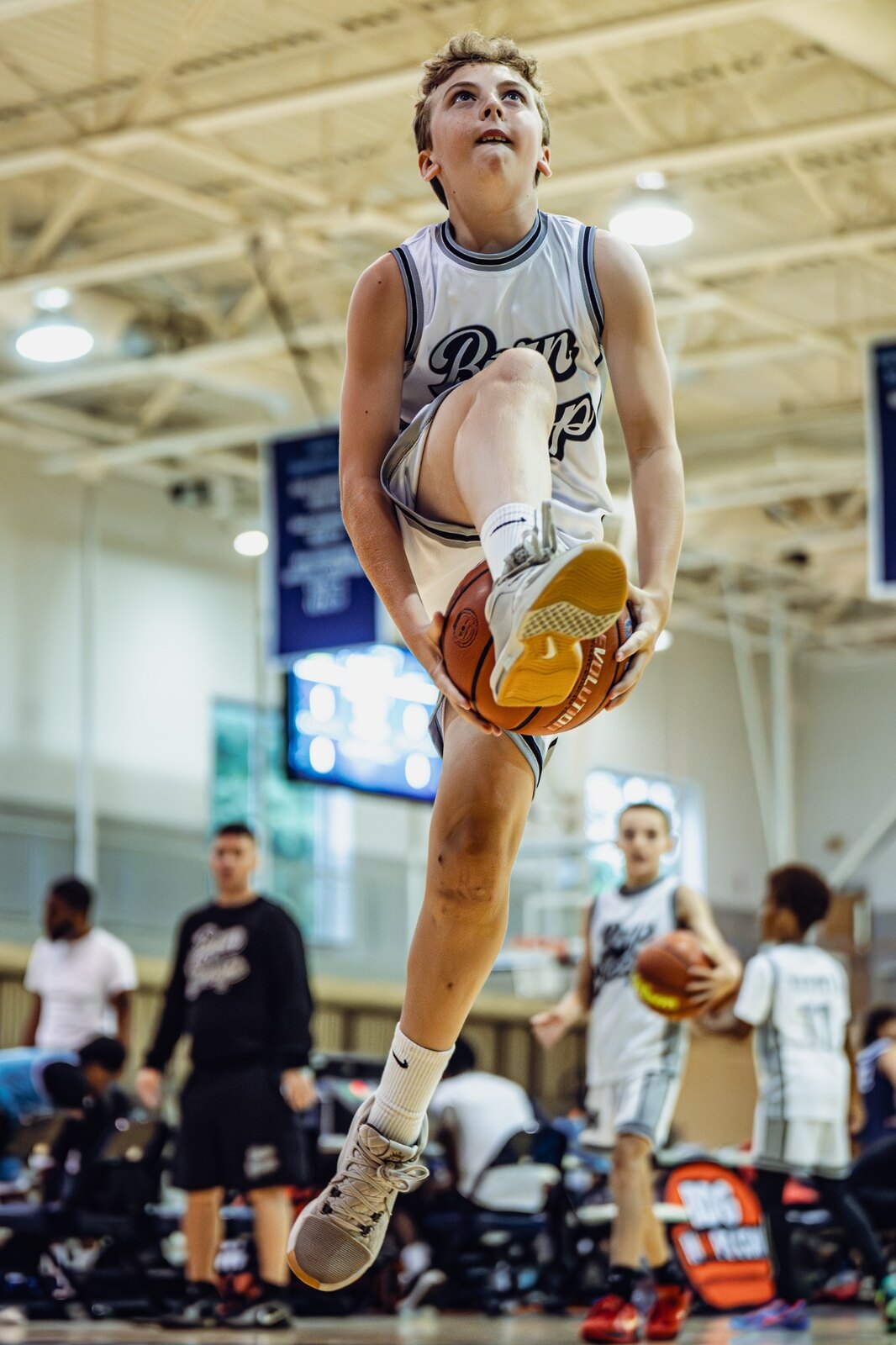 Born 2 Hoop player finishing at the rim with Coach Kevin Miller visible in the background